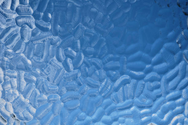 Vintage patterned frosted window glass background, blue sky and white clouds in the background.