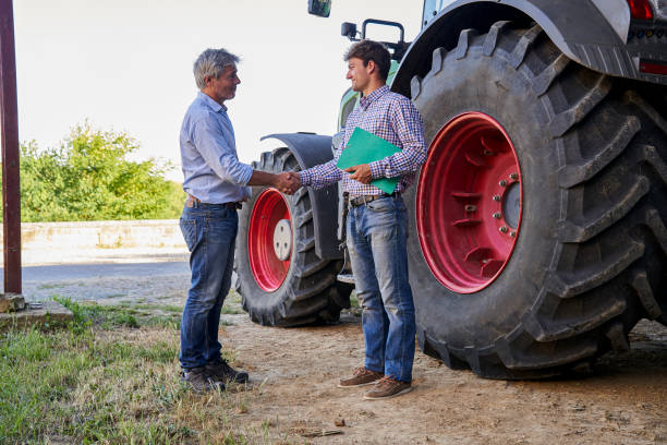 istock Agricultural advisor and farmer shaking hands while standing next to tractor inside barn 2171217200