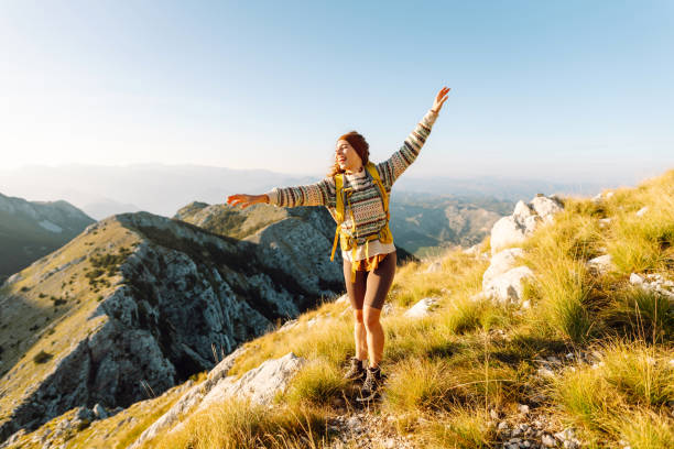 A joyful hiker enjoys the breathtaking view from a mountain summit during a sunny afternoon in the serene foothills. Nature, active life, travel.