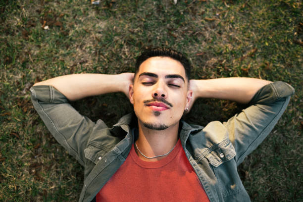 istock Young man laying down on the grass in a public park, and relaxing 2171231005
