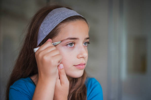Young girl tweezing her eyebrows in the bathroom