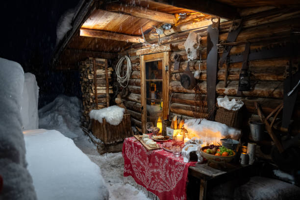 A table filled with charcuterie board items; cheese, meats and breads, outside a log cabin on a snowy evening in Winter.