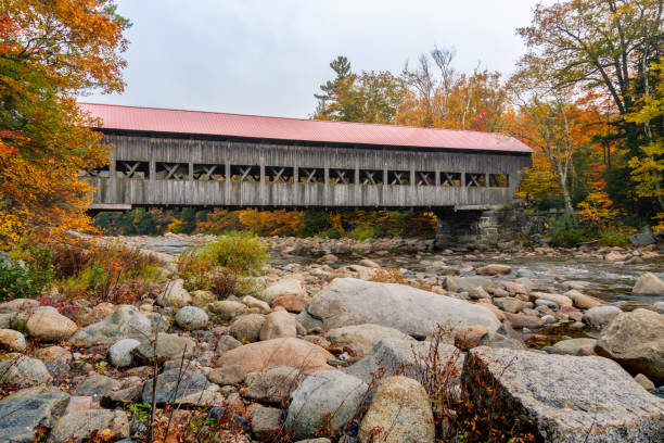 istock Underneath an active covered bridge surrounded by warm fall foliage of colorful trees, fallen leaves, big rocks and flowing water during autumn on a cloudy day 2171244053