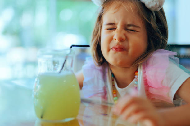 Cheerful little girl shakes hands with her first lemonade stand customer. A Caucasian man is standing in front of the stand. A jar full of coins and a basket of fresh lemons is on the stand.