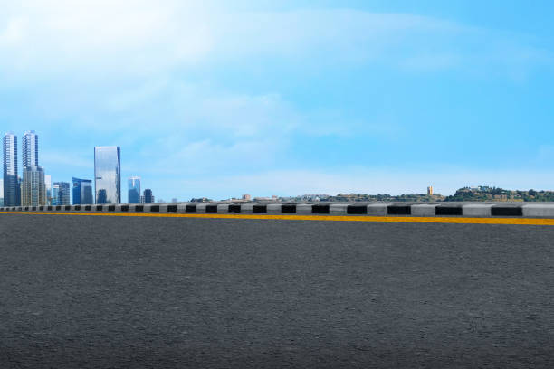 A city skyline with a large empty road in the middle. The sky is blue and the buildings are tall