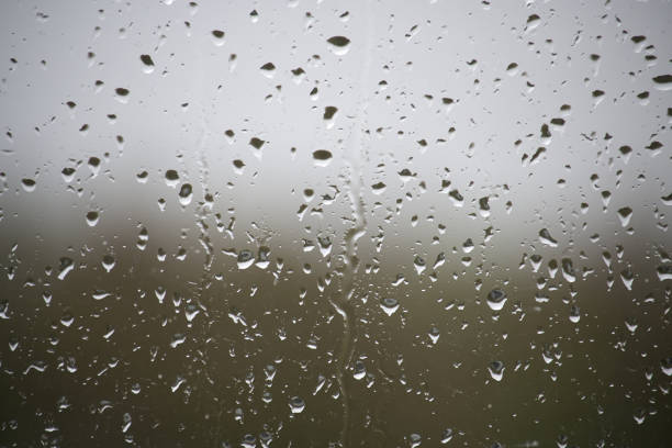 A window with raindrops on it. The raindrops are scattered all over the window, creating a blurry and hazy effect. Scene is calm and peaceful, as the raindrops seem to be falling gently