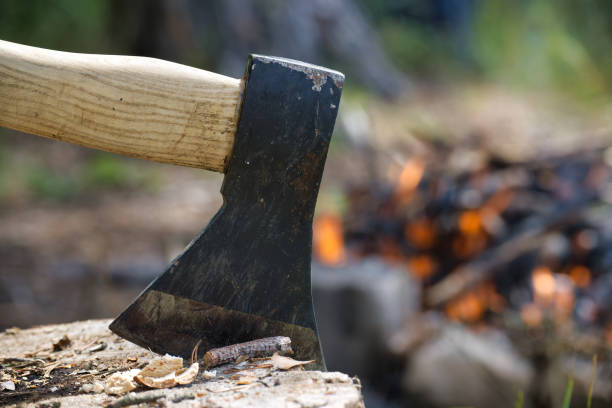istock Close-up of an axe embedded in a log with a campfire burning in the background 2171266671