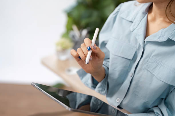 Woman Using Stylus on Digital Tablet in Modern Workspace with Green Plants in Background