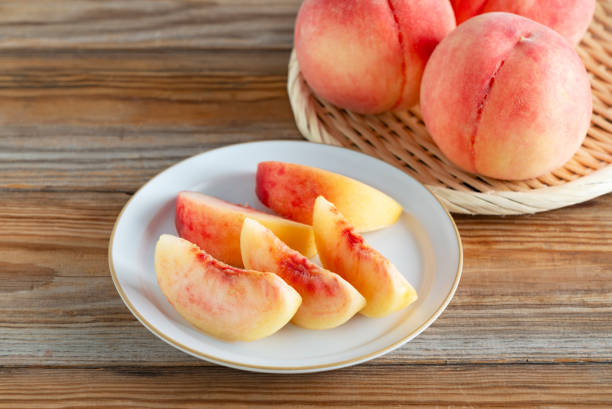 Cut Japanese peaches served on a plate on a wooden background. Image of Japanese peaches.
