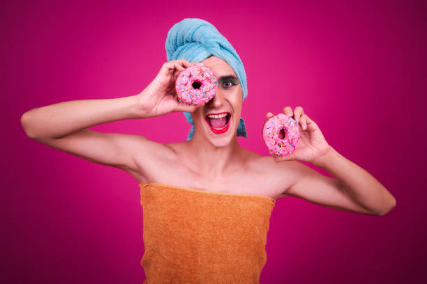 istock A funny guy dressed as a drag queen and eating pink donuts. Pink background. 2171274358