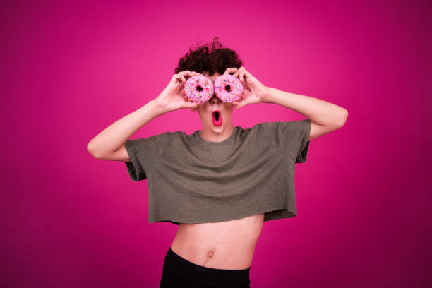 istock A funny guy dressed as a drag queen and eating pink donuts. Pink background. 2171274373