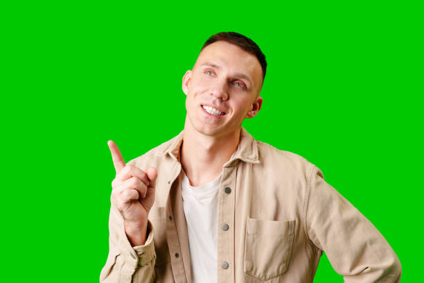 istock Young Man Pointing Upward While Smiling Against a Bright Green Background 2171278838
