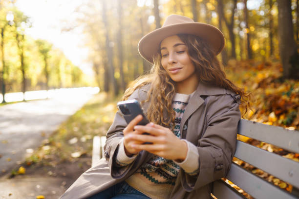 istock Young woman enjoying a sunny autumn day while texting on her smartphone in a park. 2171283861