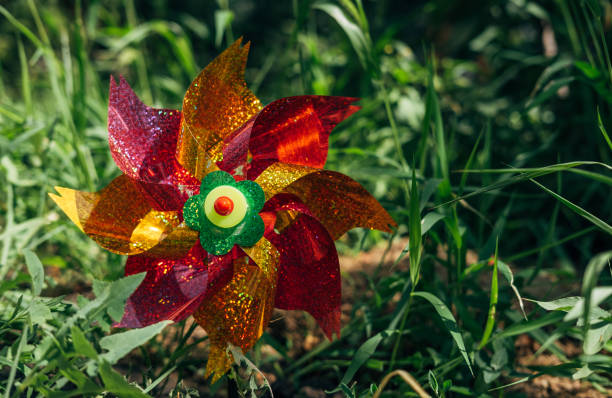 Plastic colorful pinwheel rotating, blowing by wind against the smooth green leaves surface in the garden. Toy windmill. Childhood concept