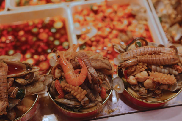 A colorful array of fresh seafood including shrimp, shellfish, and other delicacies is presented at a bustling Asian market in the evening, attracting eager customers.