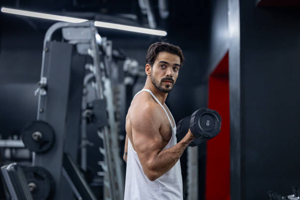 istock Caucasian beard muscular sport man is practice weight training on double dumbbells for biceps and triceps muscle inside gym with dark background for exercising and workout 2171318546