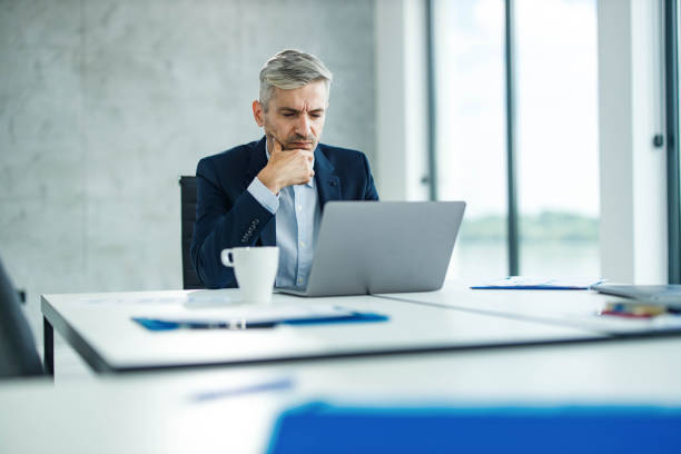 Thoughtful businessman reading a problematic e-mail on laptop in the office.