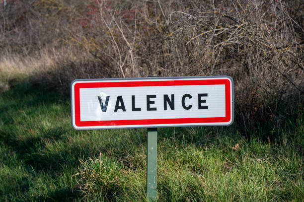 A road sign indicating the town of Valence, situated in a natural, rural setting with a backdrop of trees and grass.