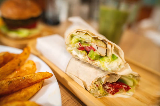 The image shows a Turkish-style meat sandwich prepared with sliced beef, tomatoes, onions and fresh herbs, all placed inside a soft flatbread. Served on a plate against a minimalist background, the dish reflects the traditional street food culture widely found in Turkish restaurants. The contrasting black and white setting helps highlight the colors and textures of the ingredients, making this composition ideal for menu layouts, branding visuals and promotional materials focused on authentic and flavorful cuisine.