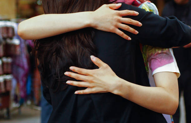 A close-up photograph capturing two people sharing a heartfelt and warm embrace, highlighting the emotional connection and support evident in their gesture, set in a public place.