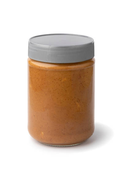 Glass jar with coarsely ground peanut butter close up on white background