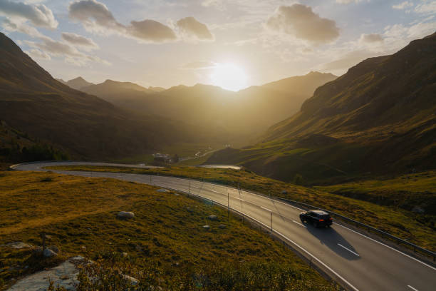 Car on scenic mountain road through Alps at sunset
