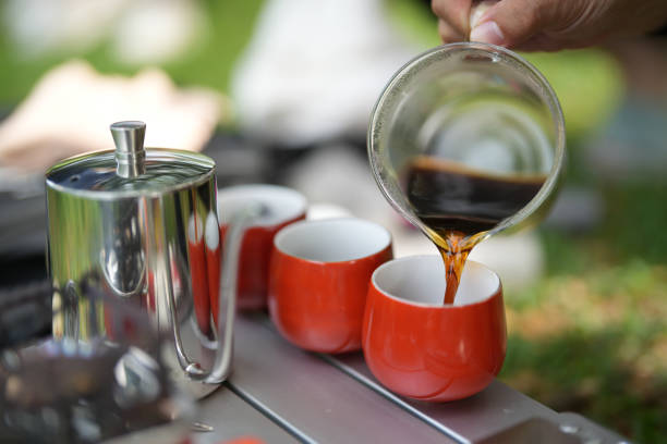 A cropped shot of a man making drip coffee on a picnic table while camping in a natural parkland in the morning.