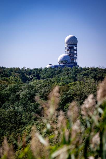 A view of the abandoned Teufelsberg listening station in Berlin, Germany, surrounded by lush greenery under a clear blue sky.
