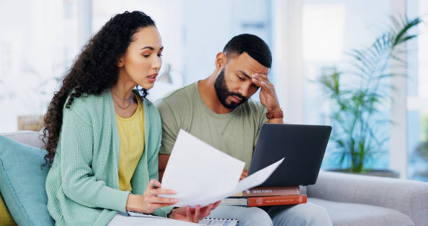 istock Frustrated couple, headache and documents with laptop for expenses, bills or financial problems on sofa at home. Young, man and woman with stress, paperwork or invoices for debt or mortgage at house 2171347543