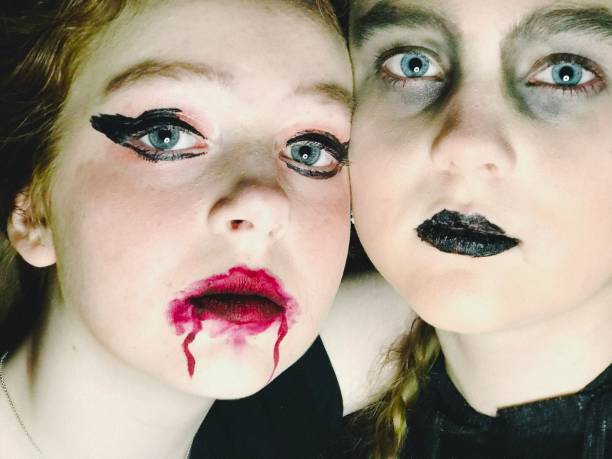 Two teens, sisters(one adopted), with painted scary Halloween faces, indoors at night, playfully posing together and bonding.