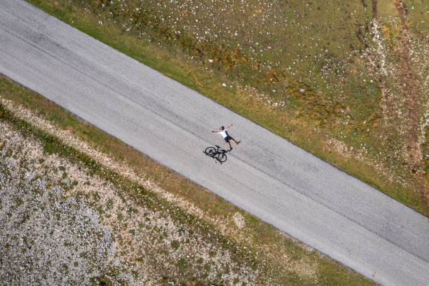 Overhead view of cheerful cyclist relaxing on an empty road in the mountain, Italy