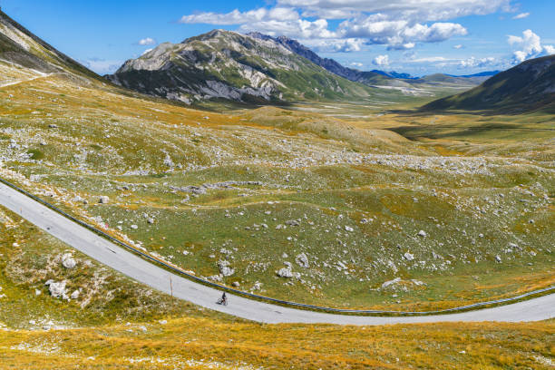 View of a cyclist riding down an empty road in the mountain landscape, Abruzzo, Italy