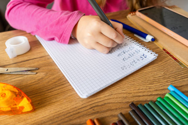 istock Child doing math exercises in notebook using smartphone with stationery on wooden table. Girl hand writing mathematical equations as school homework. Learning, education using digital tools concept. 2171352722