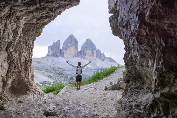 istock Hiker with arms raised, standing in cave facing mountain peaks 2171355502