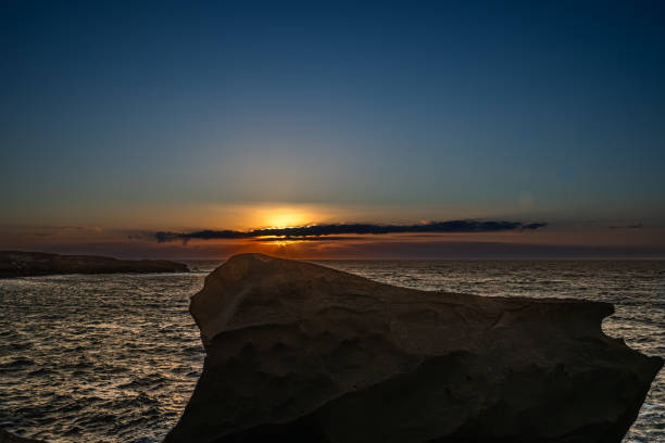 The sky is a beautiful orange color as the sun sets. The water is calm and the horizon is in the distance