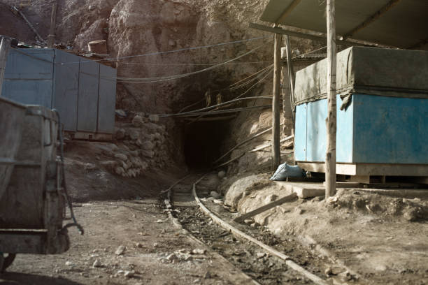The entrance to a mining tunnel with visible tracks and industrial structures in a remote, rugged landscape