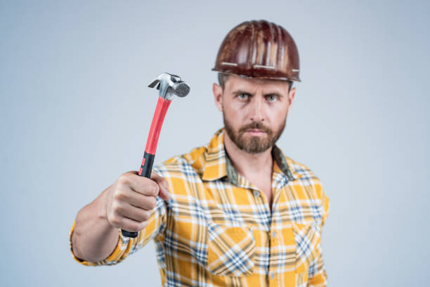 hammer in hand of man carpenter in construction safety helmet and checkered shirt on building site, selective focus, maintenance.
