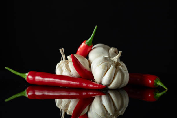 Garlic bulbs and red chili peppers on a black reflective background.