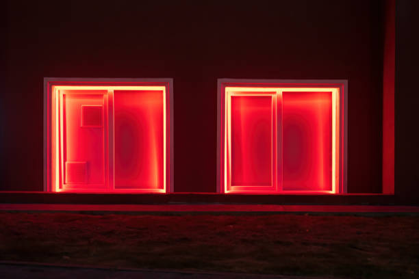 Two square windows are illuminated with red light. There is a dark wall of a building on the street in the late evening. Background.