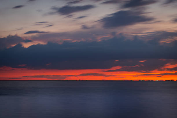 Soft pink light catching the clouds above a silky sea and sandy beach at Druridge Bay on the Northumberland coast of North East England at sunset
