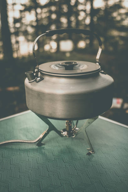 istock A silver kettle is placed on a camping stove surrounded by trees, showcasing a serene outdoor cooking setup 2171393520