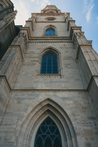 Upward view of a Gothic churchs facade with ornate windows against a blue sky.