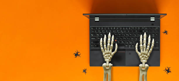Skeleton hands working on laptop, spiders nearby. Halloween concept.