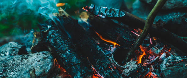 istock Vivid smoldered firewoods burned in fire close-up. Atmospheric warm background with orange flame of campfire and blue smoke. Unimaginable full frame image of bonfire. Burning logs in beautiful fire. 2171429514