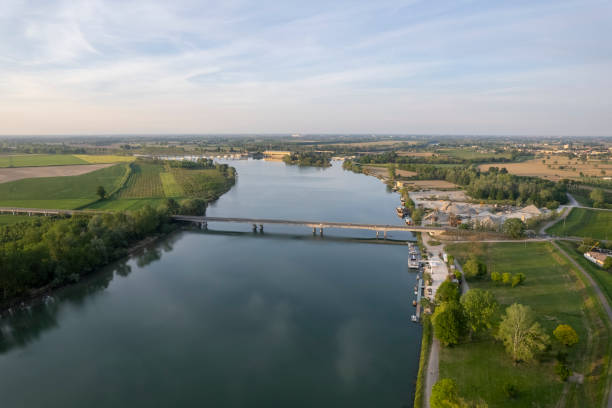 istock Bridge crossing calm river surrounded by green fields and blue sky with clouds reflecting in water 2171430389