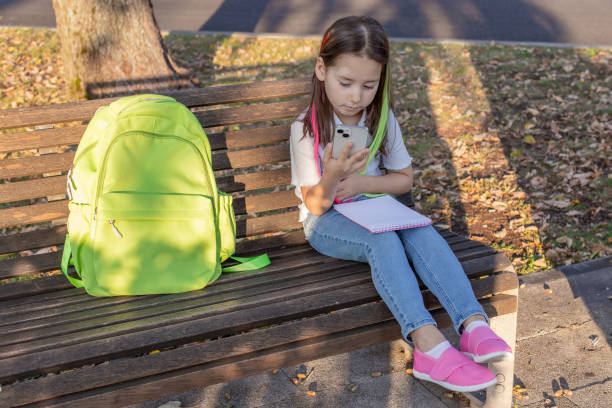 istock Young girl with smartphone and backpack on park bench in autumn setting 2171439473