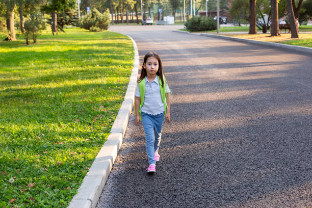 istock Young girl walking along park path with backpack in sunlit morning 2171441642