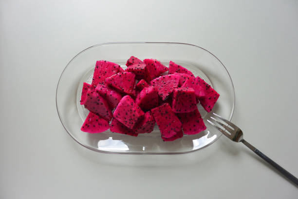 Cut red dragon fruit with fork on glass plate. Gray color background. Top view.
