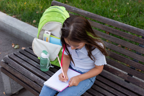 istock Young girl writing in notebook on park bench with backpack and water bottle 2171443752