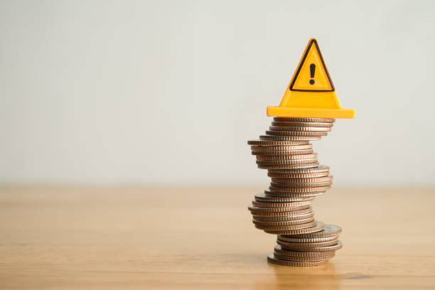 istock Warning sign label on stack coins in uncertainty situation on wooden table with white background copy space. 2171450213